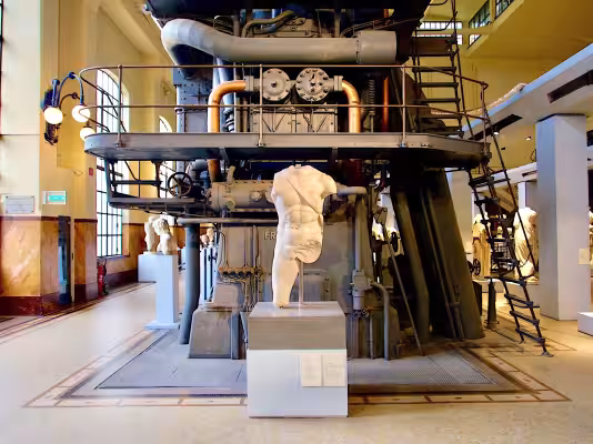 A marble statue in front of industrial machinery at Centrale Montemartini